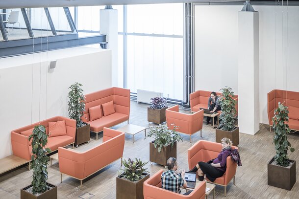 Impact HUB Personen sitzen auf orangen Polstermöbeln.