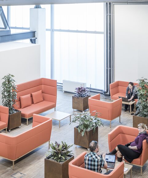 Impact HUB Personen sitzen auf orangen Polstermöbeln.