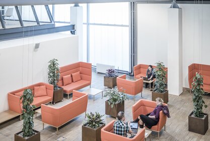 Impact HUB Personen sitzen auf orangen Polstermöbeln.