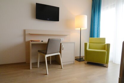 Room with a brown chair and green lounge seating.