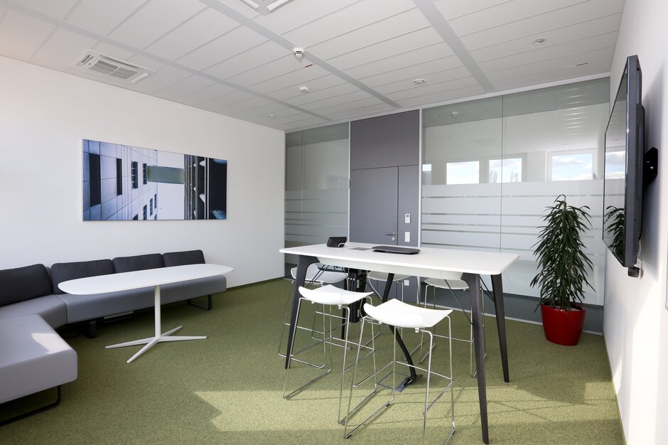 TÜV Austria Salle de réunion avec tabourets de bar blancs et meubles rembourrés gris.