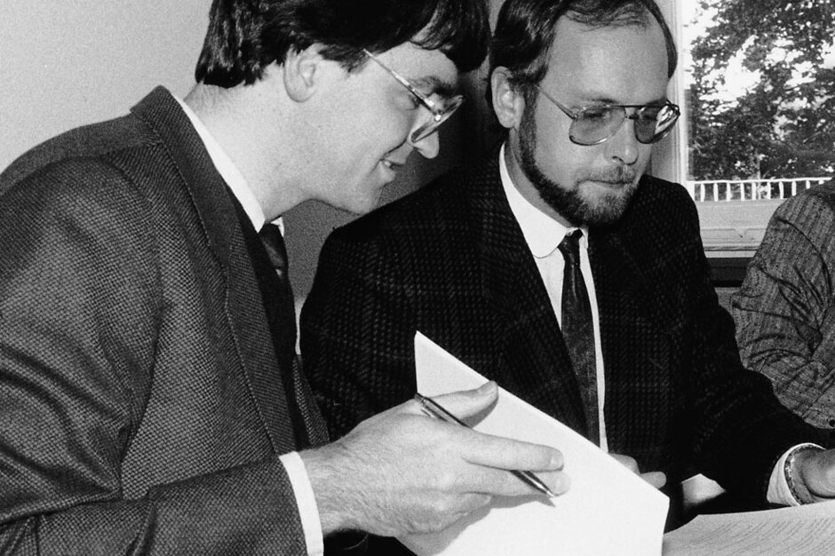 Black and white photo of two people signing a contract.