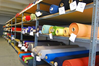 Different colored rolls of fabric on a shelf.