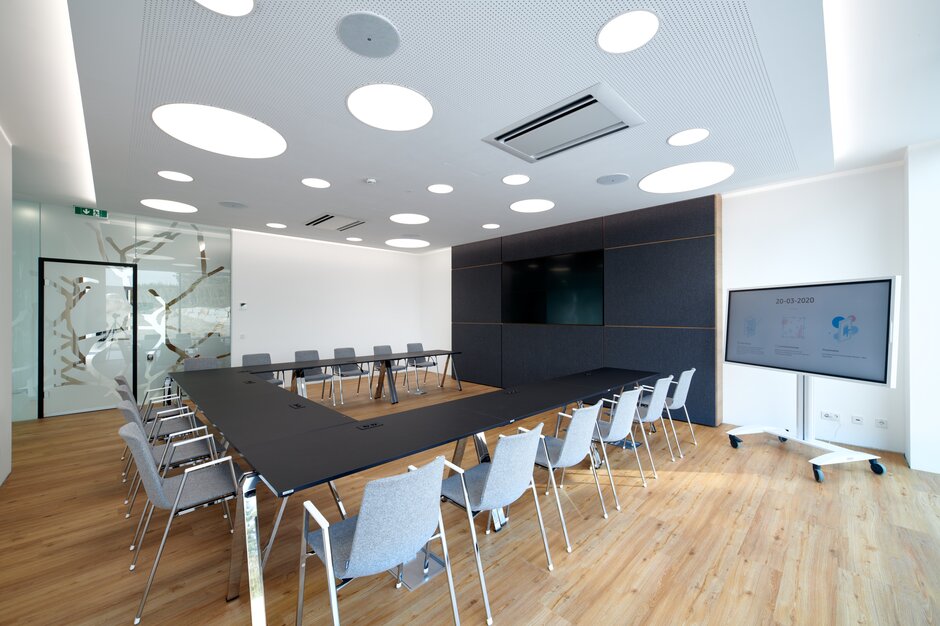 Großer Konferenzraum für Meetings und Konferenzen mit schwarzem Konferenztisch und grauen Stühlen.