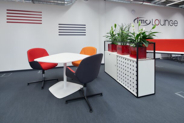 Des chaises rouges et orange devant une table blanche avec un cabinet blanc. | © raumpixel.at