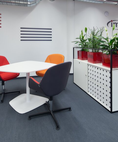 Des chaises rouges et orange devant une table blanche avec un cabinet blanc. | © raumpixel.at