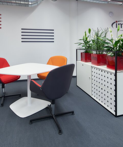 White bistro table with colourful conference chairs and a white cabinet. | © raumpixel.at