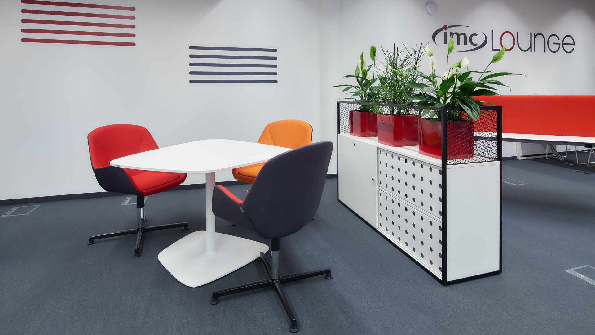 Des chaises rouges et orange devant une table blanche avec un cabinet blanc. | © raumpixel.at