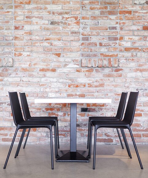 Schwarzer Tisch mit schwarzen Stühlen vor einer Backsteinwand.