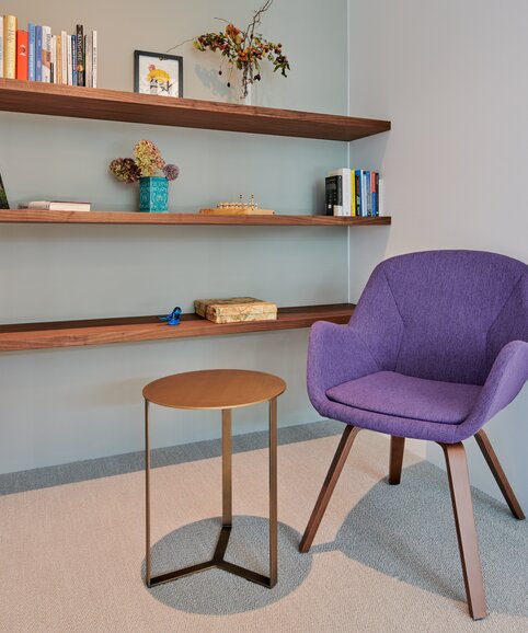 Violetter Stuhl vor einem Bücherregal aus Holz. | © raumpixel.at