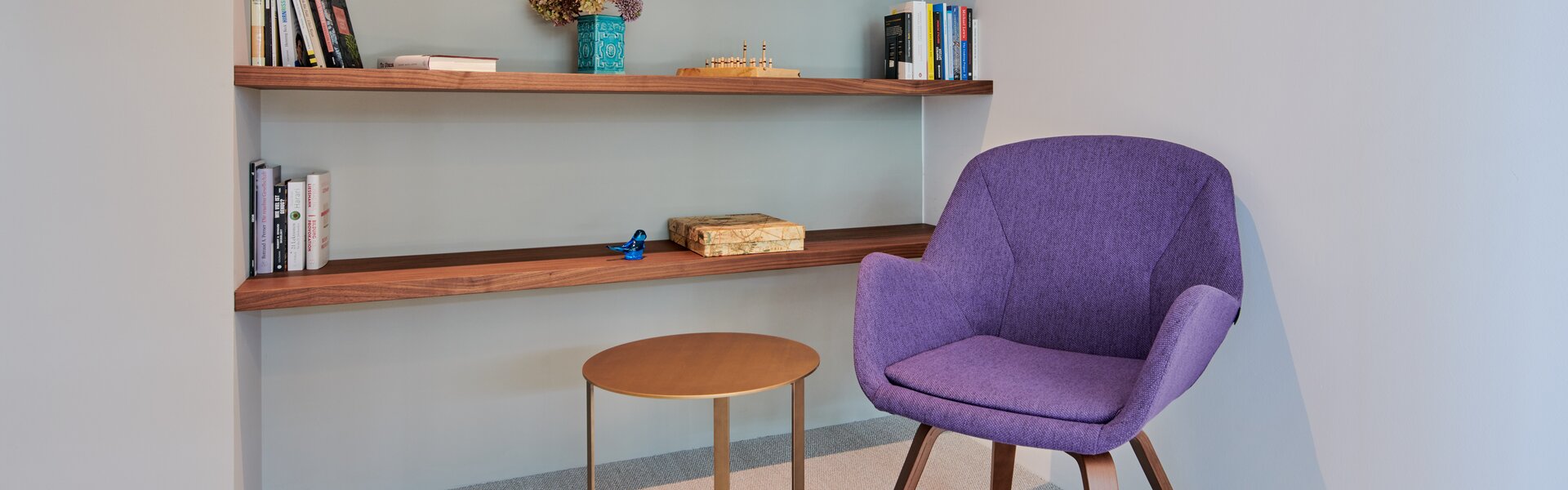 Violetter Stuhl vor einem Bücherregal aus Holz. | © raumpixel.at