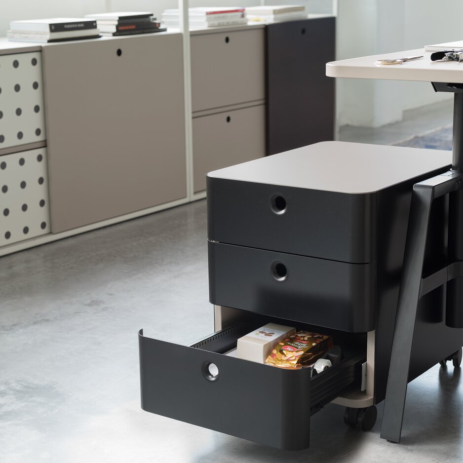 un conteneur à rouleaux noir avec trois tiroirs dont 1 ouvert à côté d’un bureau avec une armoire coulissante à l’arrière-plan