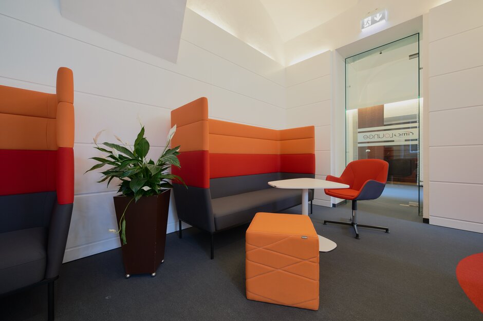 Lounge area with red and orange lounge seating and white bistro tables. | © raumpixel.at