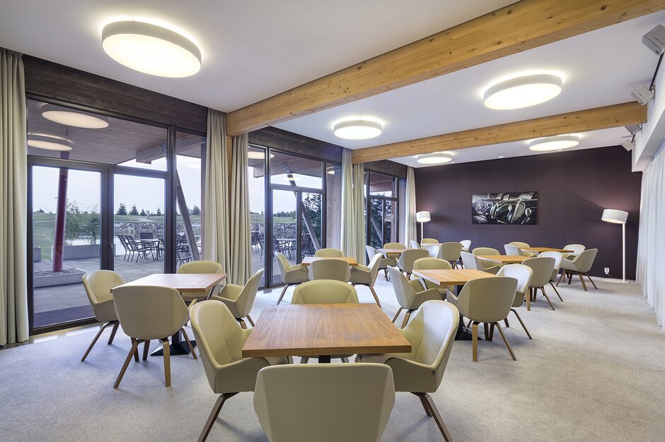 Golfresort Mladá Boleslav tables en bois et chaises beiges devant un mur en verre