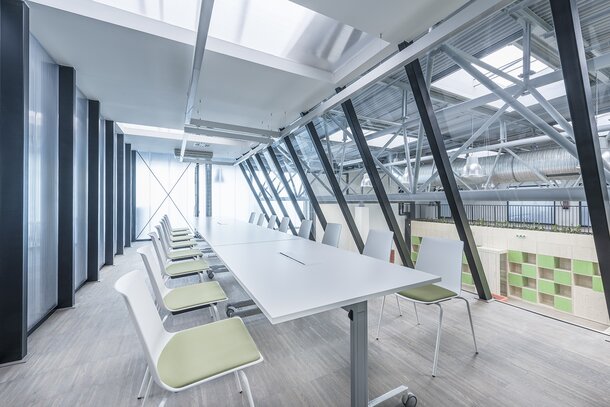Impact HUB Weißer, langer Tisch und weiße Stühle mit grünem Bezug.