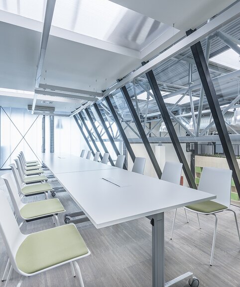 Impact HUB Weißer, langer Tisch und weiße Stühle mit grünem Bezug.