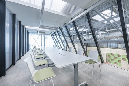 Impact HUB Weißer, langer Tisch und weiße Stühle mit grünem Bezug.