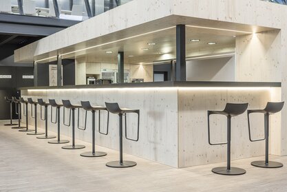 Impact HUB Schwarze Barstühle an einer Bar aus hellem Holz.