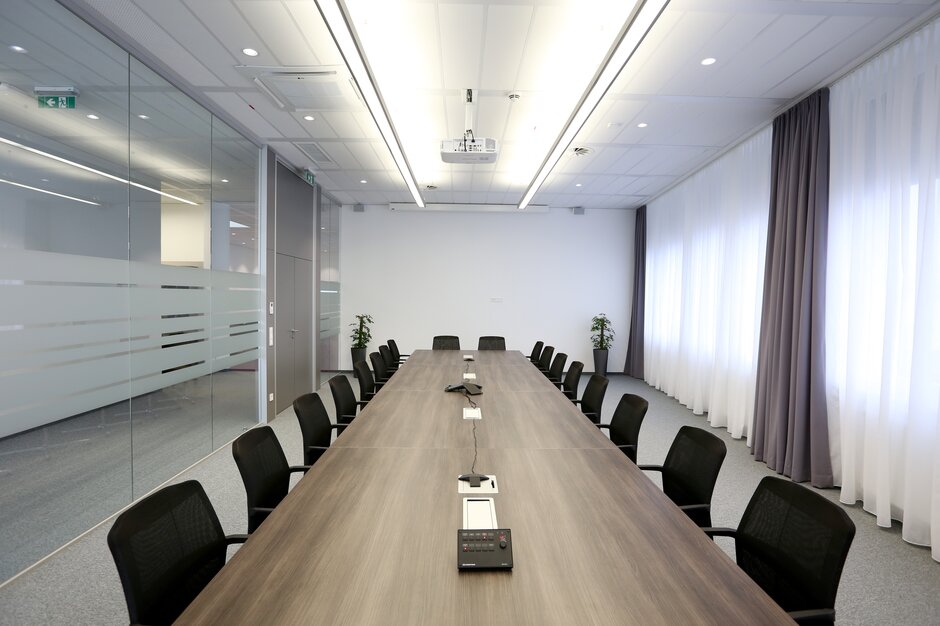 Konferenzraum mit dunklem Konferenztisch und Konferenzstühlen.