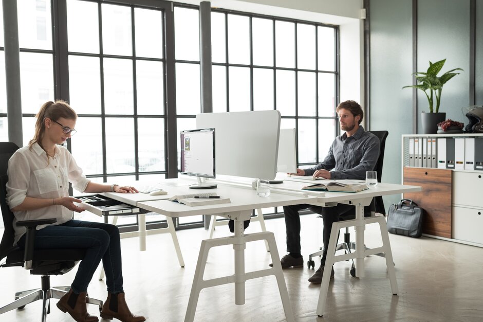 Two people sitting in an office with a white office desk for two person. 