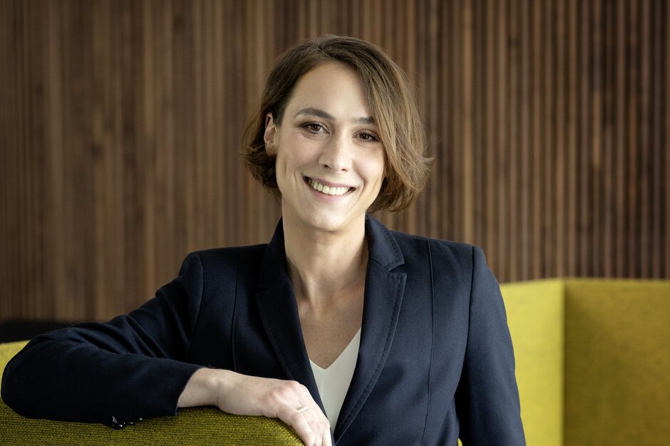 Porträt Laura Wiesner Laura Wiesner lehnt an gelbem Polstermöbel.